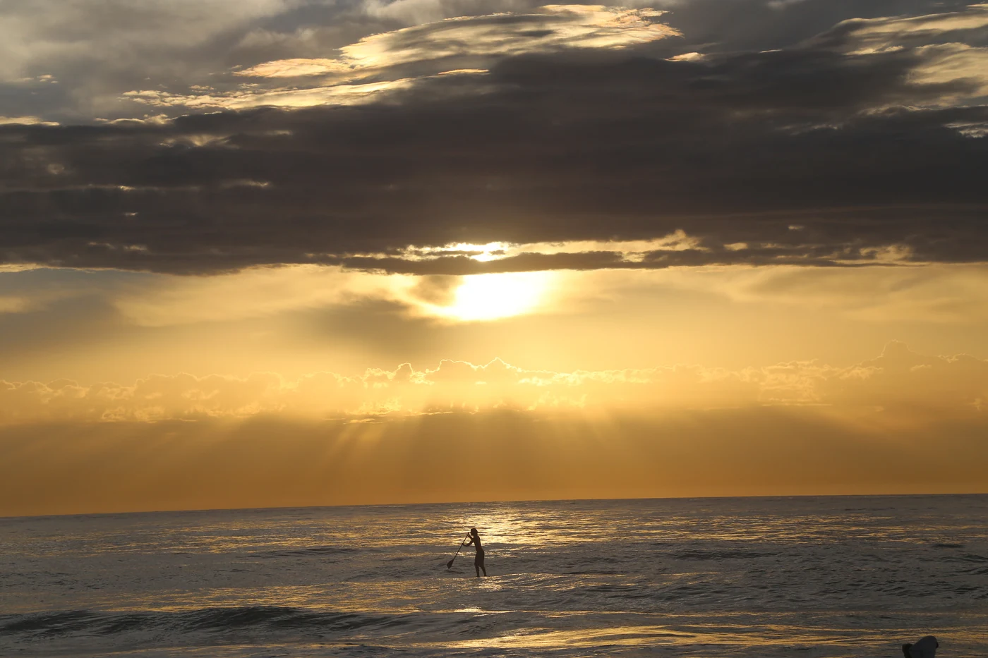 Osamělý paddleboardista na klidné hladině moře při východu slunce.